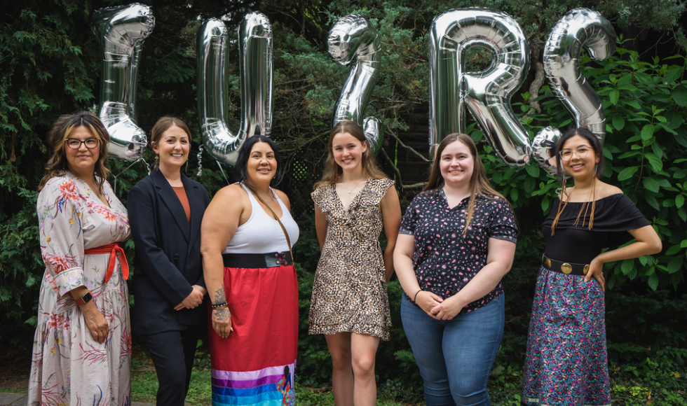 Indigenous Undergraduate Summer Research Scholars program (IUSRS) participants Nicole Bouchard, Brittany Skov, Bonita Bohnet, Hannah Butterworth, Hannah Thomas and Aleria McKay standing outdoors smiling at the camera. Behind them there are five large balloons spelling out ‘IUSRS.’