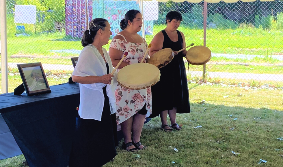 Three people in dresses playing Indigenous drums.