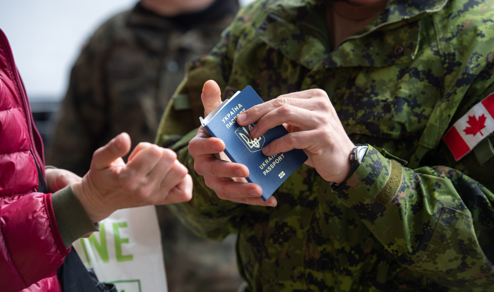 A tight shot of a Canadian Armed Forces member’s hands holding a Ukrainian passport. The CAF member is in military fatigues and a Canadian flag can be seen on their arm.