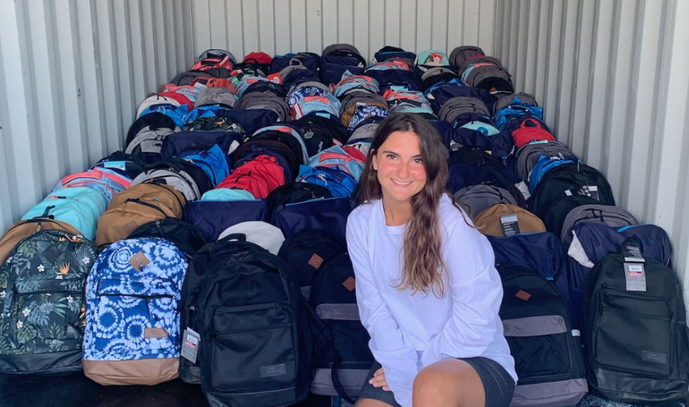 Blerina Ago sitting in a storage container full of backpacks smiling at the camera.