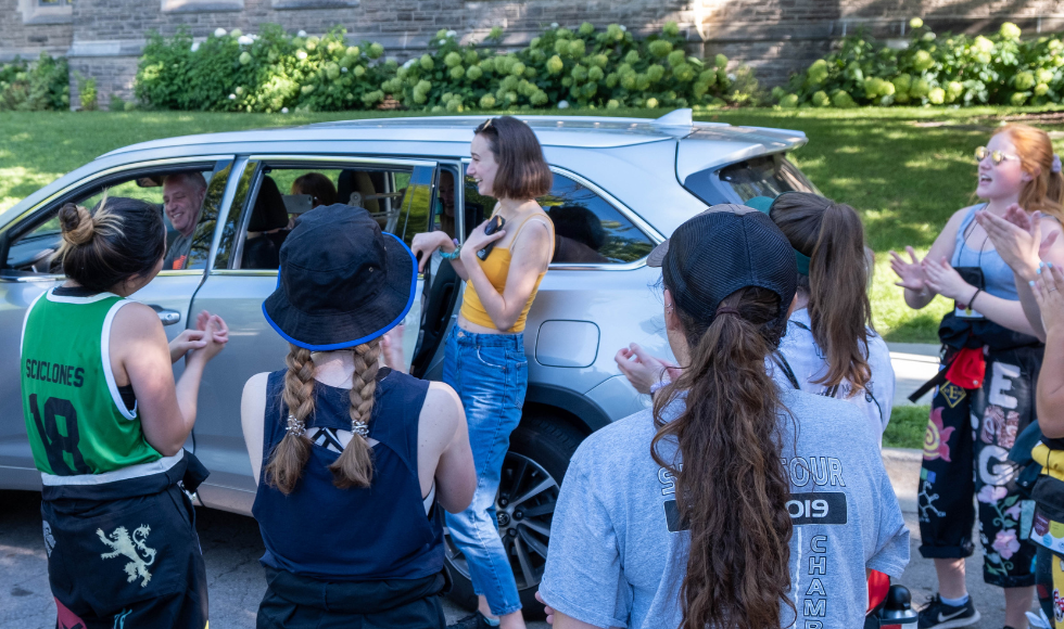 A student is greeted by Welcome Week reps on McMaster’s campus as they step out of a car.
