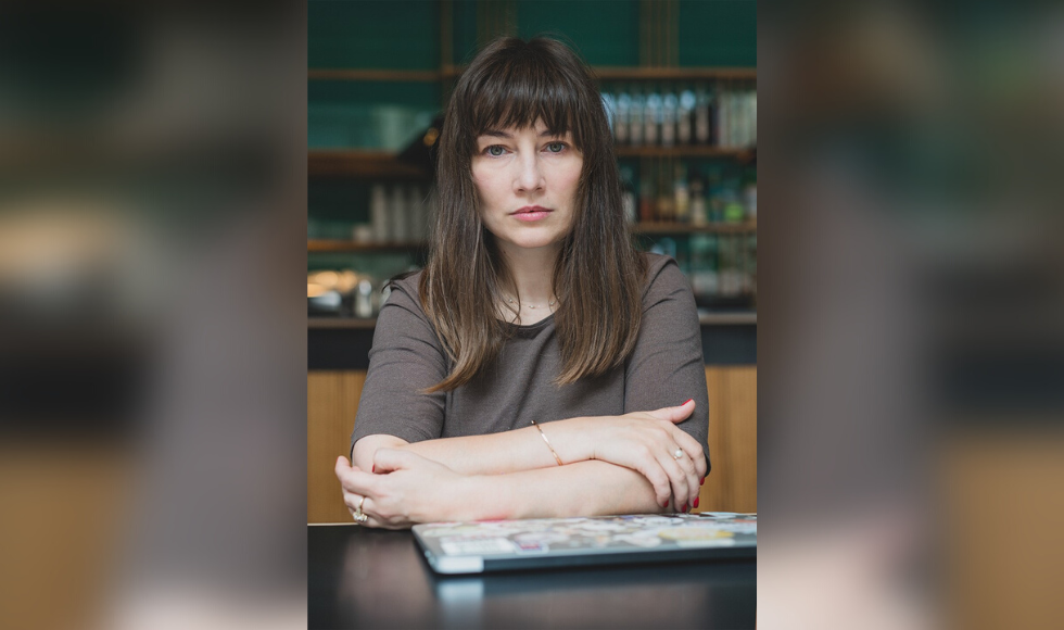 Kateryna Babkina seated at a table with a closed laptop in front of her. She is looking directly at the camera and not smiling.