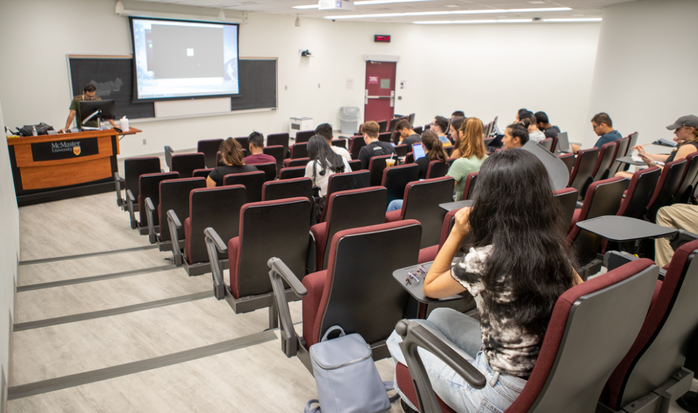 Students seated inside a classroom while an instructor speaks at the front of the room