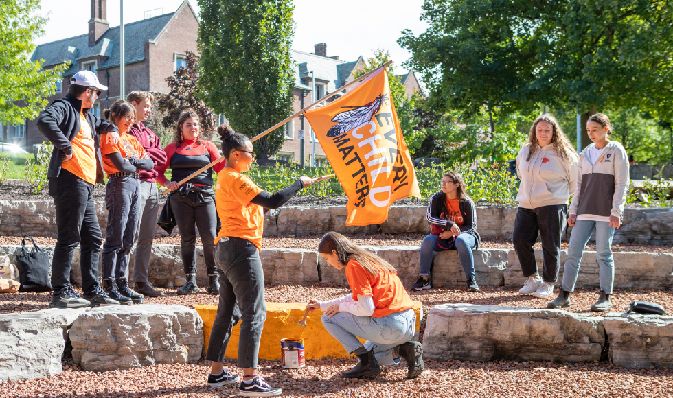 Group of people in orange T shirts panting a large stone orange.