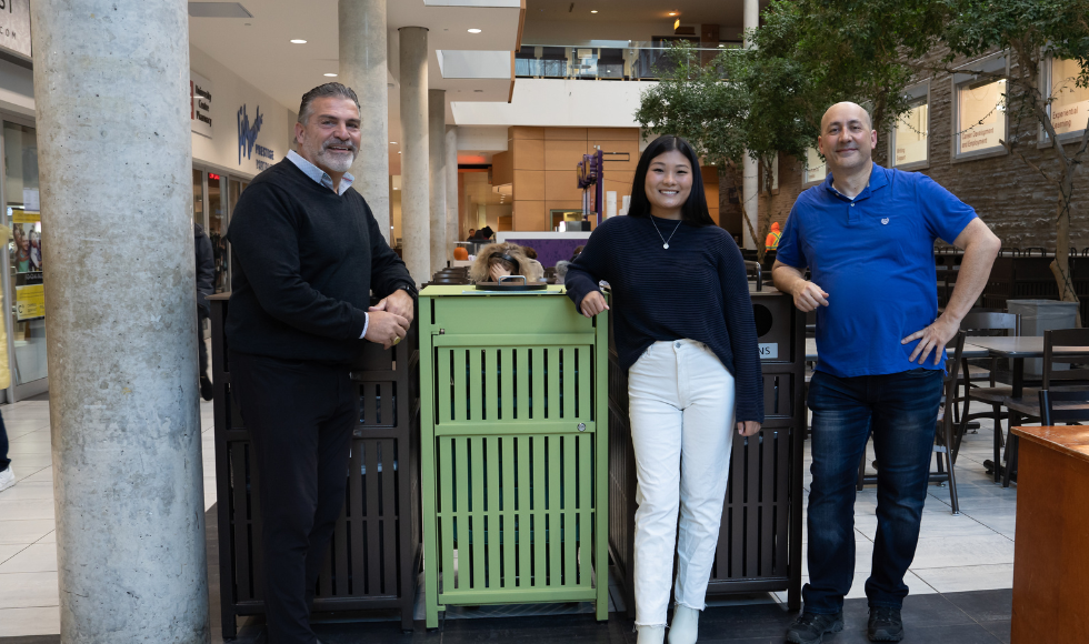 3 people leaning against disposal bins beside the seating area in MUSC.