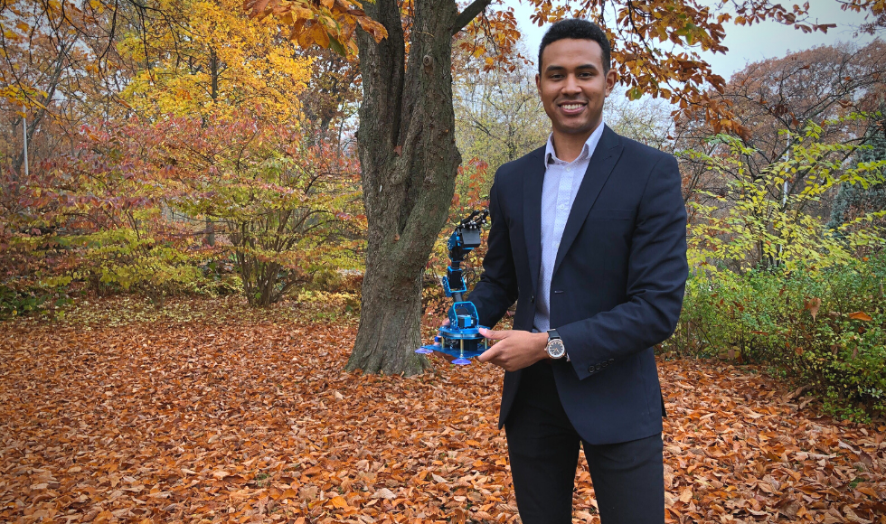 Michael Jobity standing outdoors holding the robotic arm he developed.