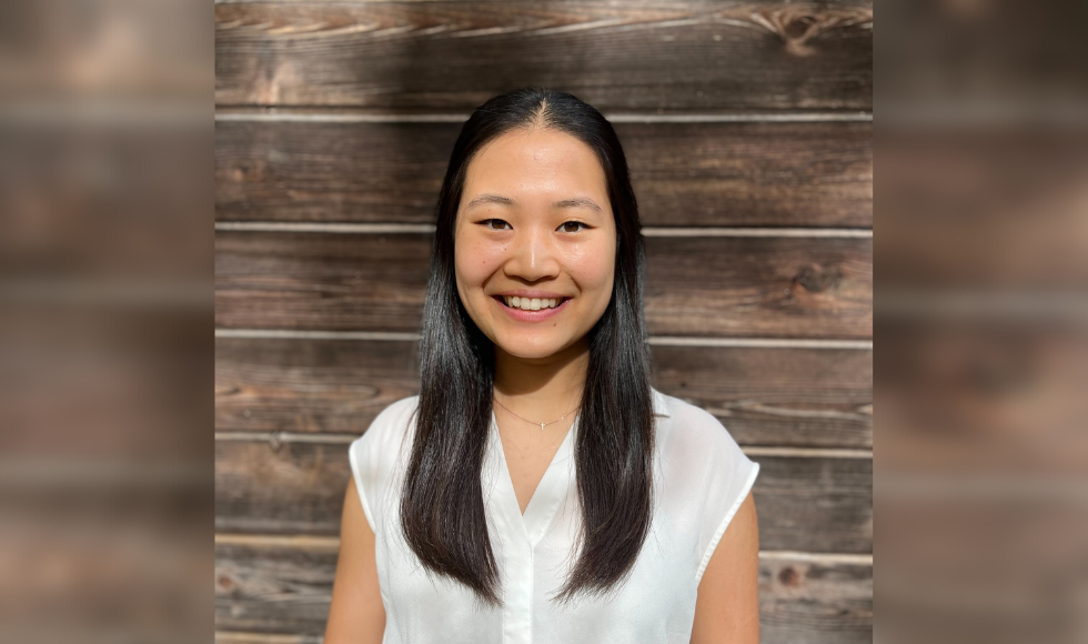 Smiling Paris Liu head and shoulders standing in front of a wood backdrop. Her hair is long and dark and she is wearing a while blouse.