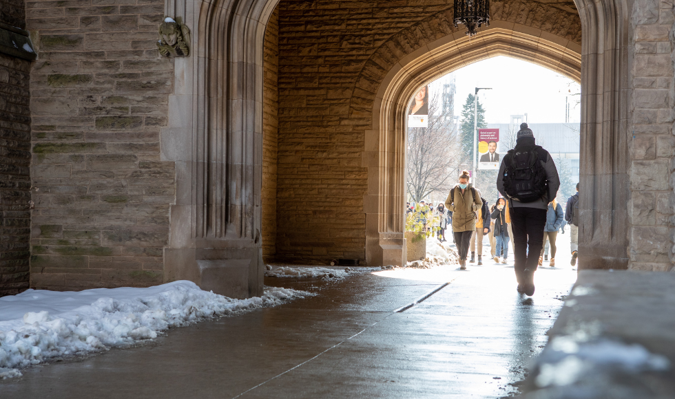 Students walk through the University Hall archway on McMaster's campus on a sunny, snowy day