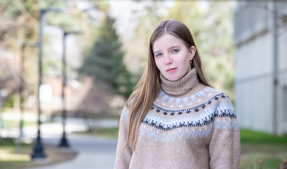 Olga, a woman with long brown hair, wearing a turtleneck sweater outdoors on campus.