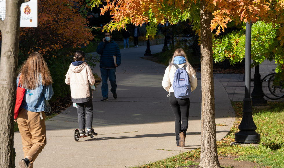 Students seen from behind as they walk down a tree-lined path on campus in the fall.