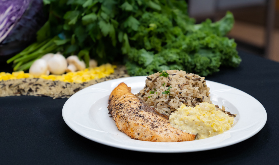 Sumac salmon plated with wild rice and corn in a white dish on a black tablecloth