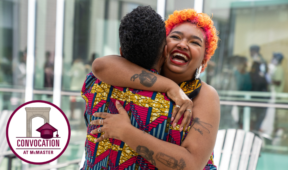 Graduating student Candace Walkes laughs as she hugs her sister Samantha, whose back is toward us. In the corner is a 