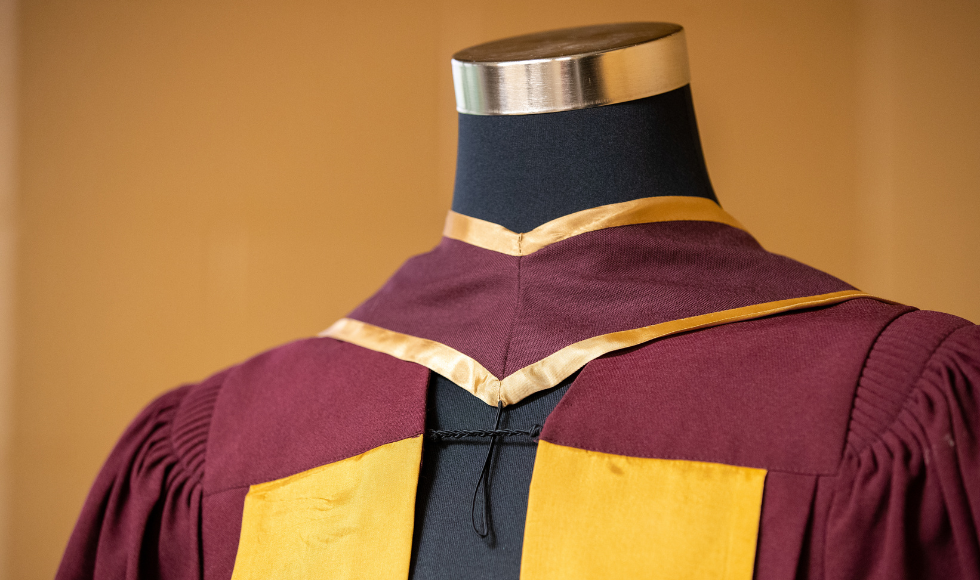 A maroon and gold convocation robe on a headless mannequin