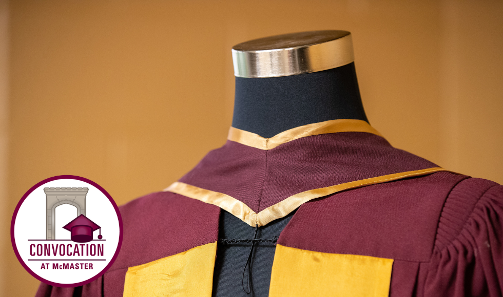 A maroon and gold convocation robe on a headless mannequin, with a sticker that reads: Convocation at McMaster