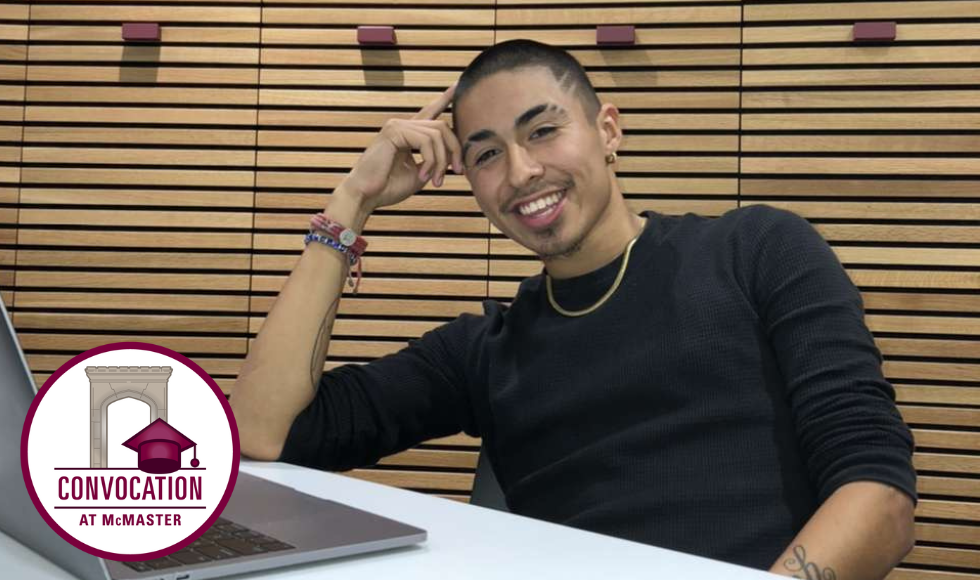 Ian-Carlo sitting at a desk in front of a laptop, leaning his head on his hand and smiling.