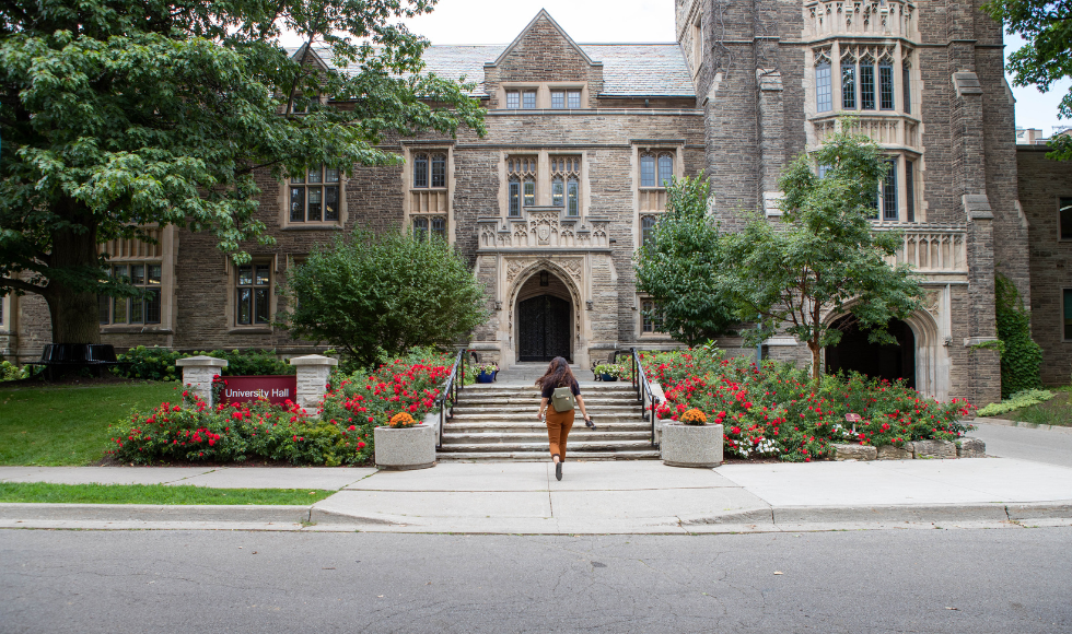 A student with their back to the camera heading up the steps to McMaster's University Hall