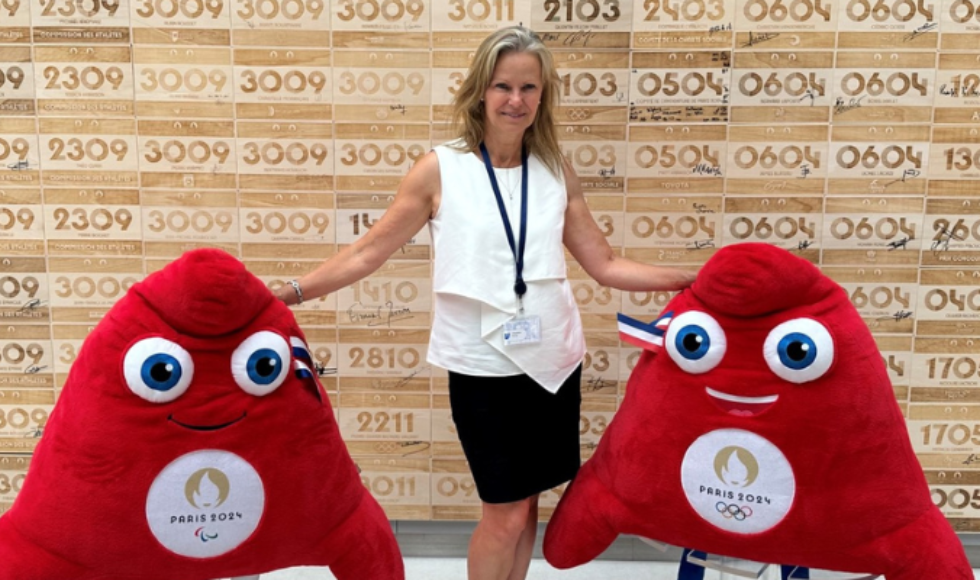 Margo Mountjoy posing for a photo with two red, plush Paris 2024 mascots