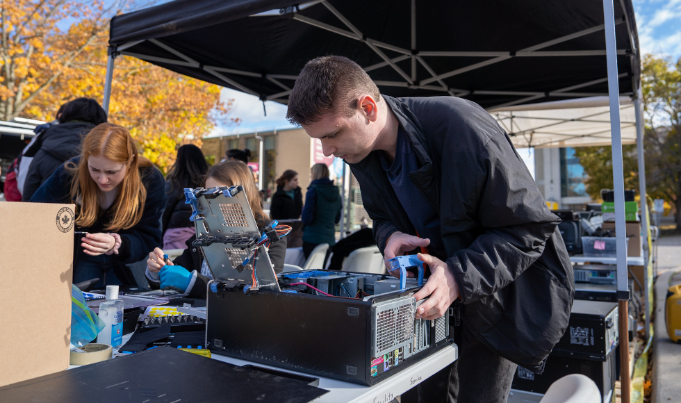 A student leaning over a computer tower that is lying on its side on a table