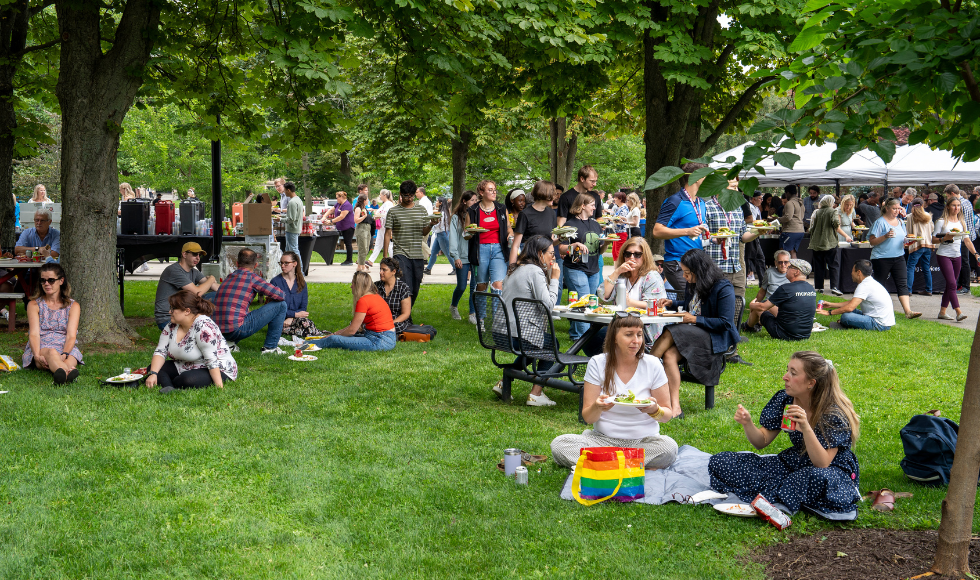 people sitting, standing, chatting, eating, laughing on BSB field during the employee BBQ