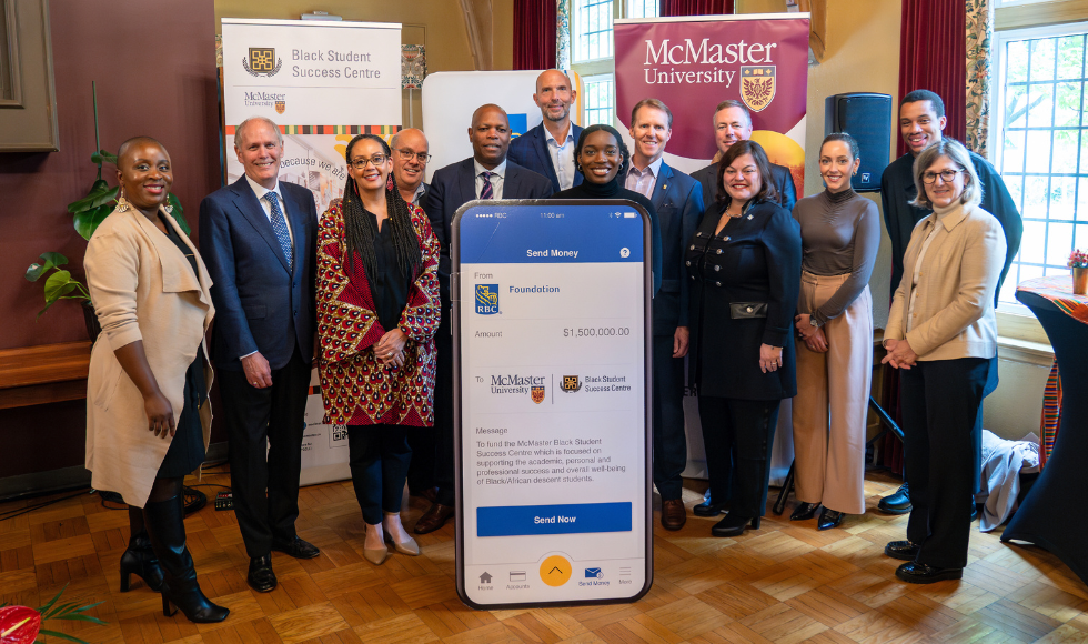 A group of people standing with a large replica of a cellphone screen that has the RBC and McMaster University logos on it.