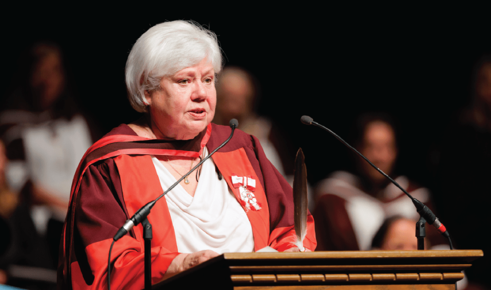 Pat Mandy dressed in convocation regalia speaking at a podium