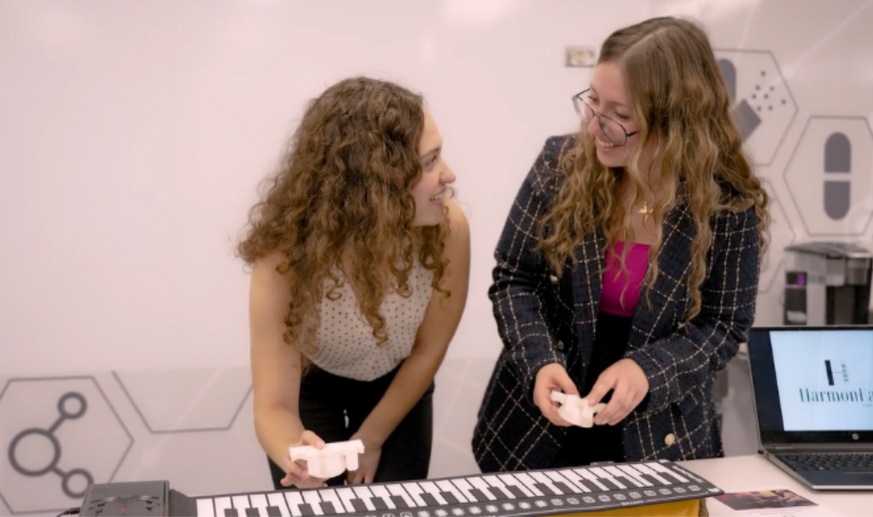 Lianna Genovese and Deena Al-Sammak smile at each other while standing at a musical keyboard.