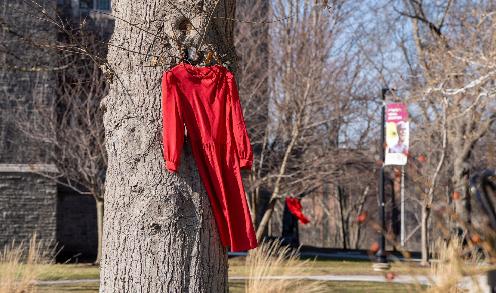 A red dress on a hanger hangs from a tree on campus.