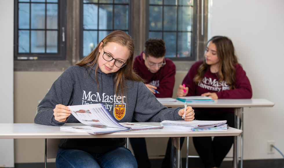 Three students - all wearing McMaster University branded clothing - studying at desks.