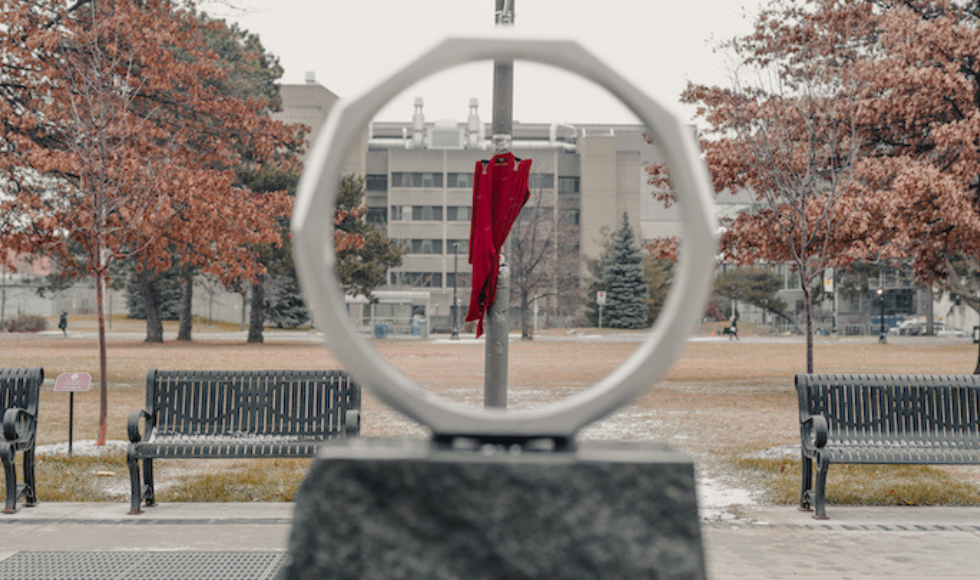A red dress hanging on McMaster's campus, seen through the centre of an iron ring sculpture.
