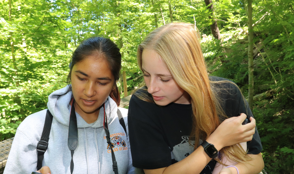 Shania Ramharrack-Maharaj and Kate Pearson out on the Cootes trail, looking down at a device