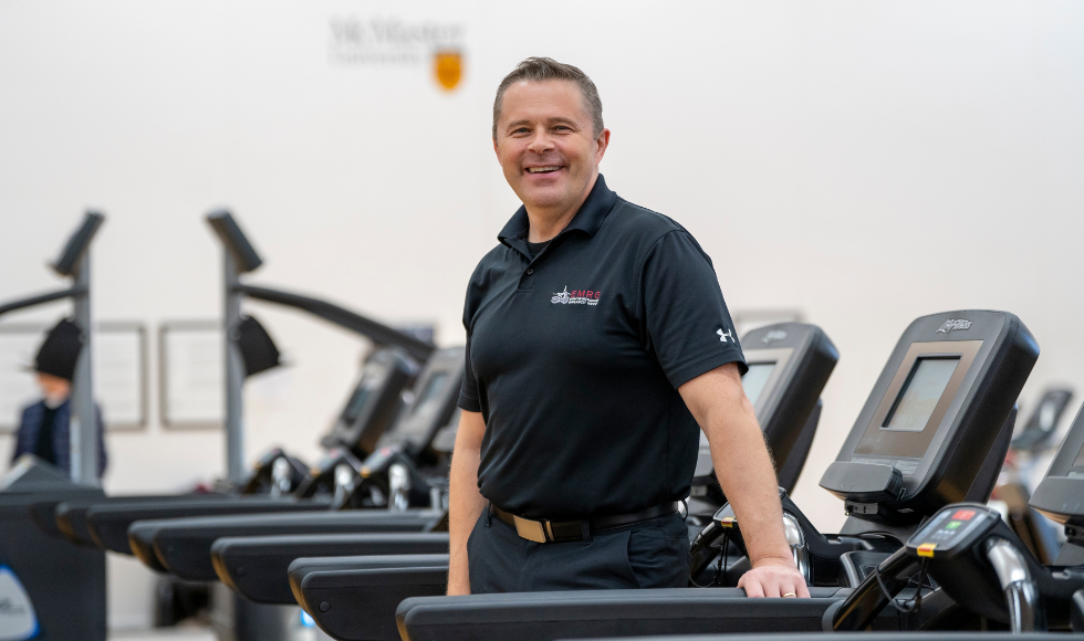 Stuart Phillips standing in side a room filled with exercise equipment while smiling at the camera