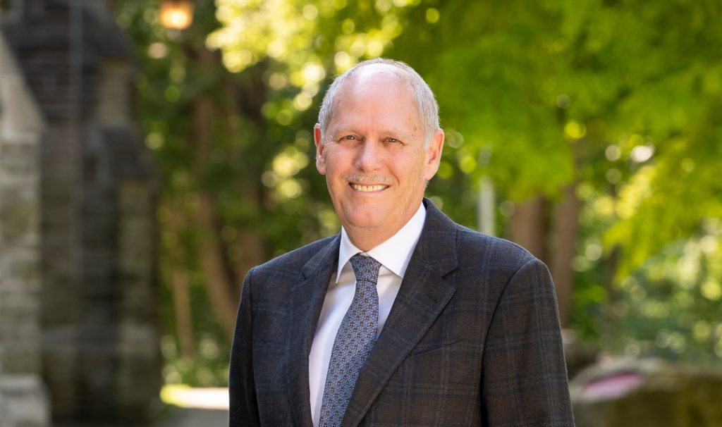 Head and shoulders of smiling David Farrar in a suit, standing outdoors in the shade on a sunny day at McMaster