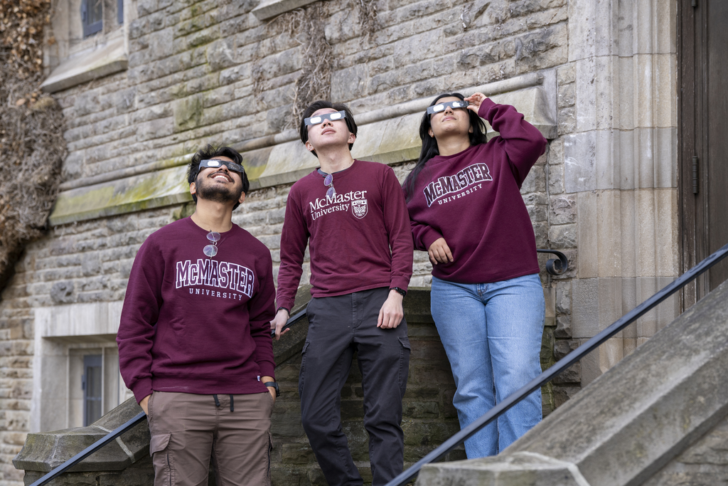 Three students with their solar glasses on looking up to the sky