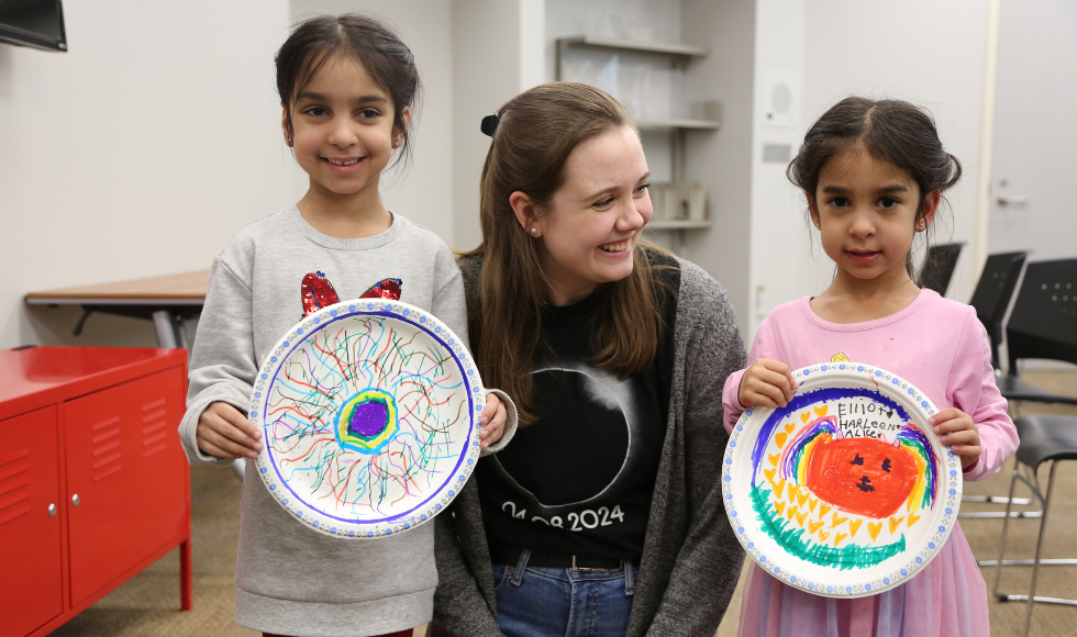 Nicole Mulyk posing for a photo with two young girls who are holding decorated paper plates