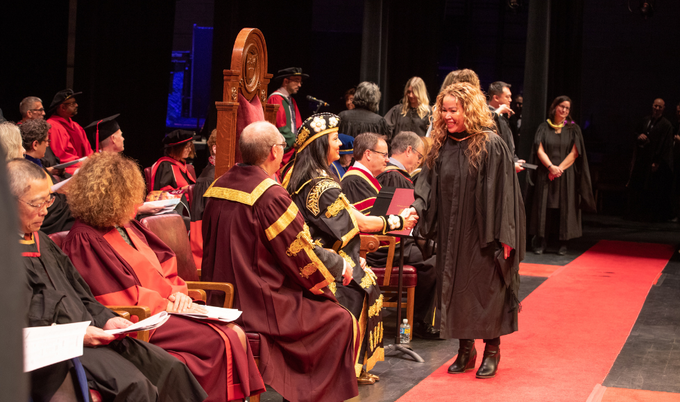 A graduate shakes the hand of McMaster's Chancellor as they cross the convocation stage