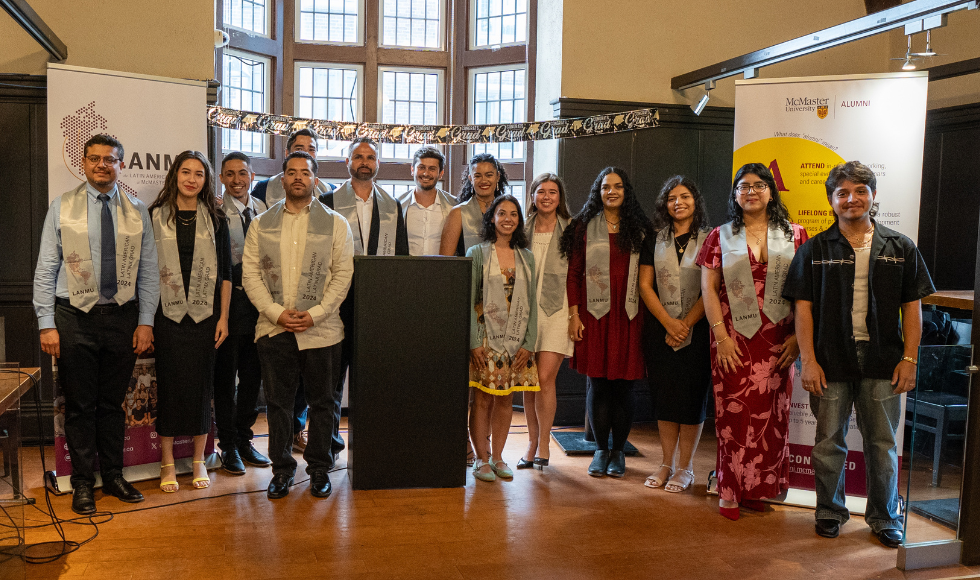 14 people standing on a stage smiling at the camera. All but one are wearing convocation stoles.