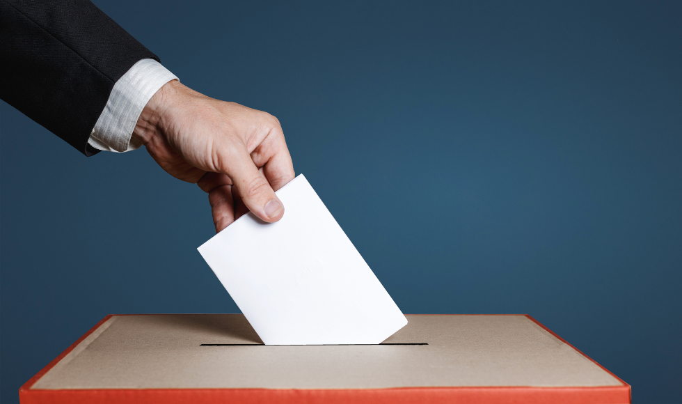 A hand putting a folded piece of paper into a ballot box