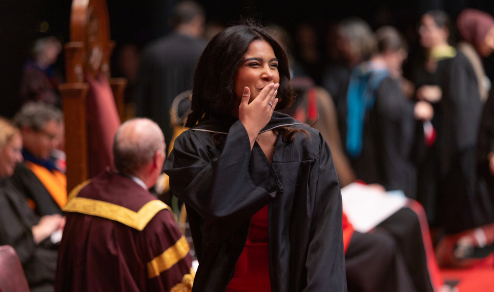 A person in a graduation gown blowing a kiss as they cross a Convocation stage
