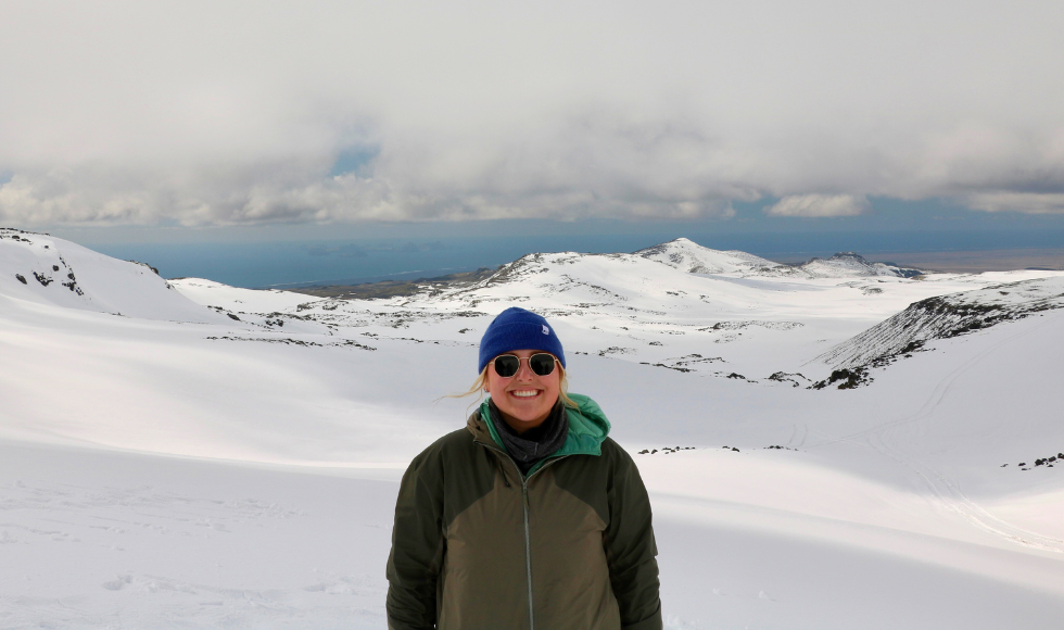 Brooklyn Ambis standing in front of a series of snowy mountains. There is a body of water far in the distance behind her.