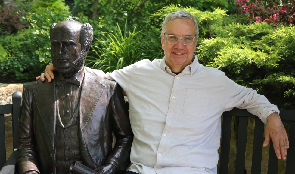 Jeff Goodes sitting on bench with his arm around the statue of Senator William McMaster