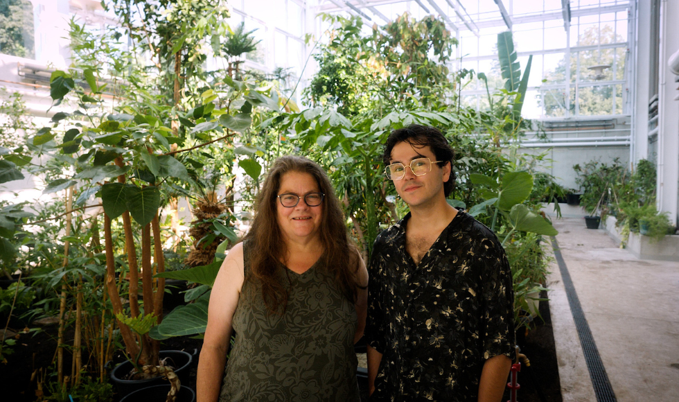 Two people standing in front of greenery looking directly at the camera