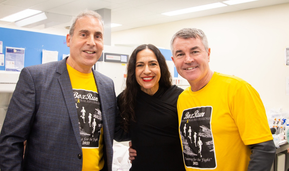 Three individuals standing side by side. The two people on the sides wear t-shirts with “Box Run” graphics, while the person in the centre is dressed in black.