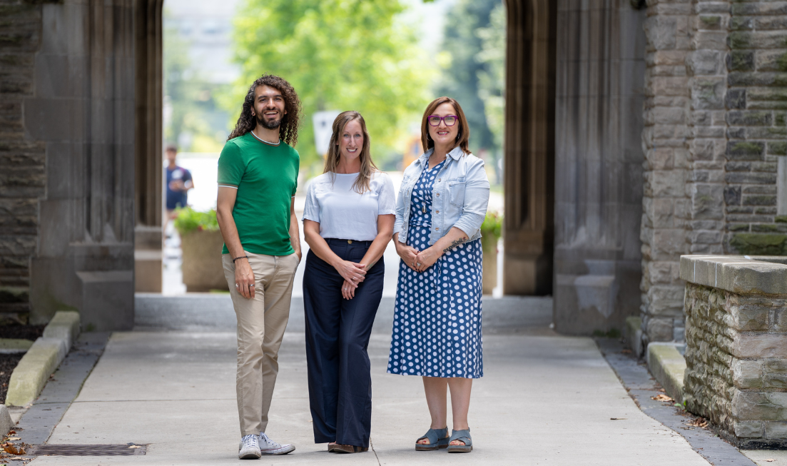 Three people standing near the University Hall Arch at McMaster.