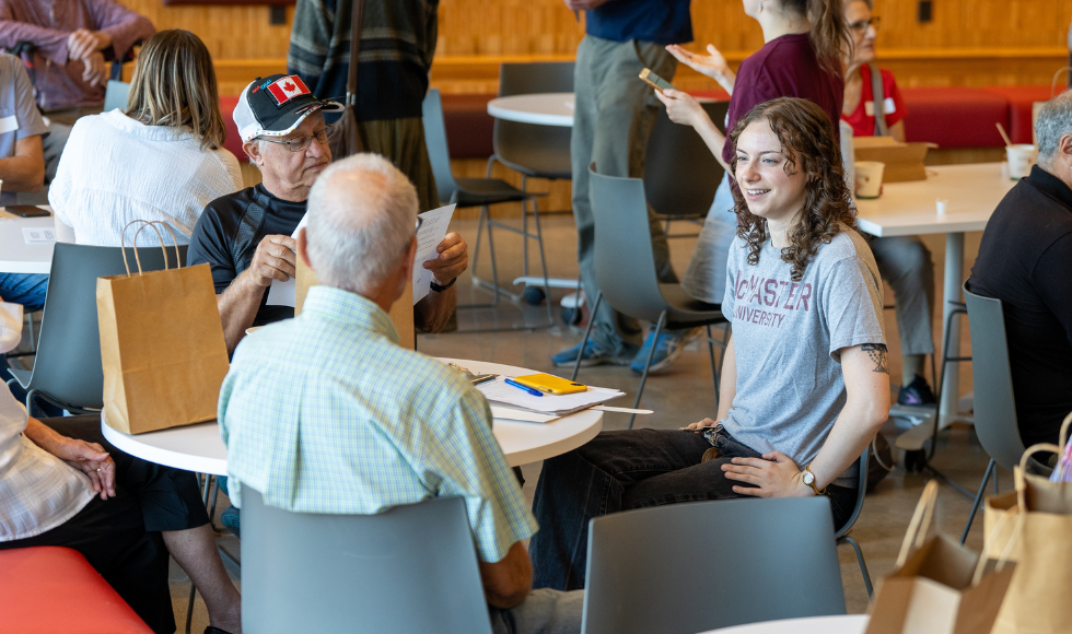 A student in a McMaster t-shirt seated at a table engaged in conversation with two older adults