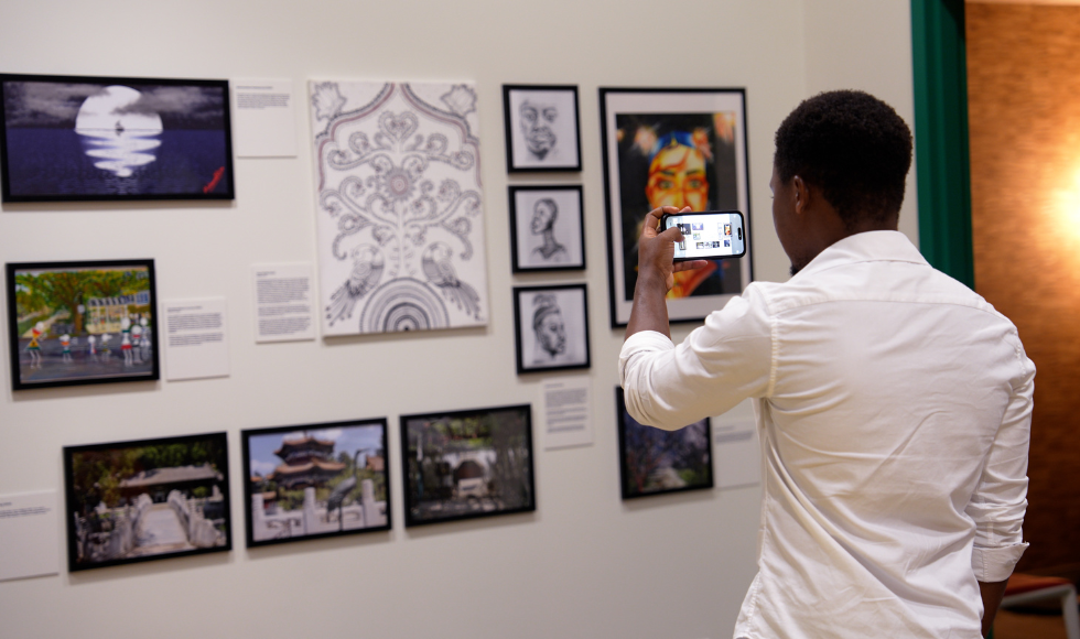 A person with their back to the camera using a cellphone to take a picture of a wall of art