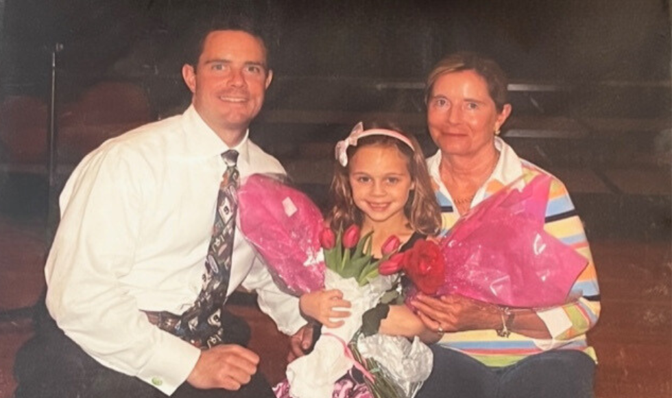 Three people — a man, a woman and a young girl smiling at the camera. The young girl is holding a bouquet of pink tulips.