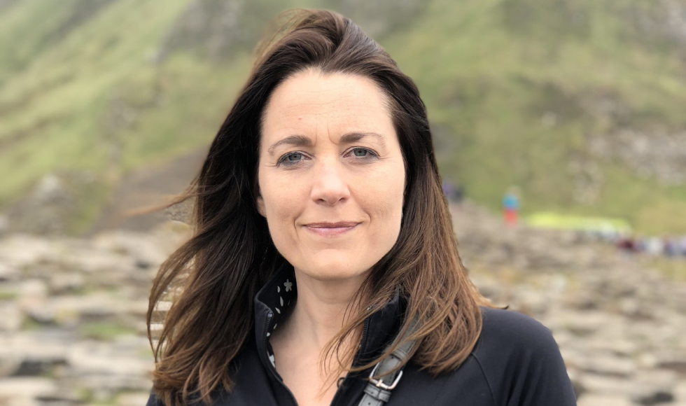 A tight shot of Kristina Llewellyn's face as she looks directly at the camera. Behind her is a rocky landscape that is out of focus.