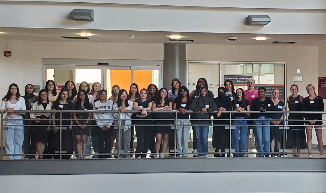 A group of more than two dozen students standing in the school of Rehabilitation Sciences at McMaster.