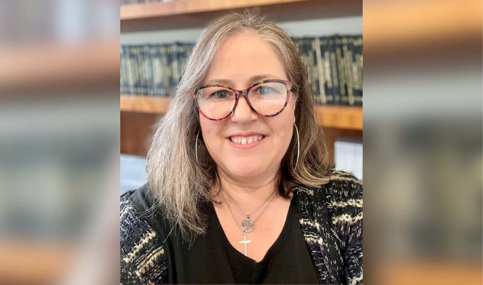 A headshot of smiling Paula Marcoux against a backdrop of bookshelves.