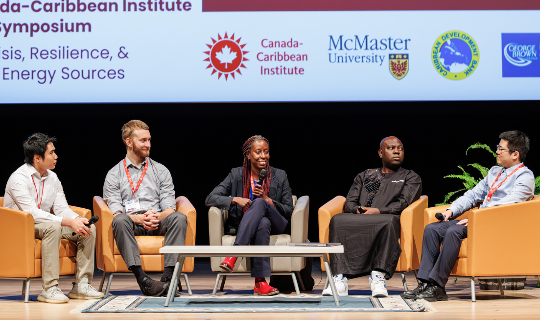 Five student researchers sit in a row of armchairs on stage during a panel discussion